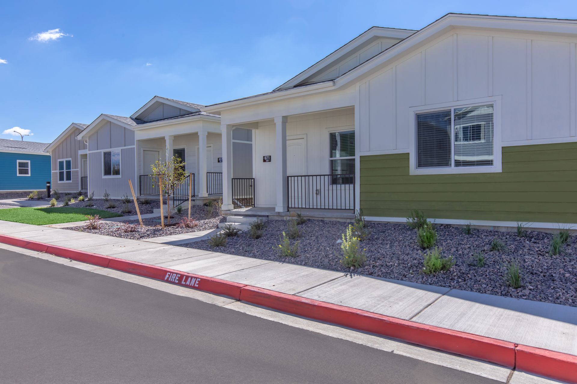 Row of modern single-story houses with white siding and green accents beside a red curb.