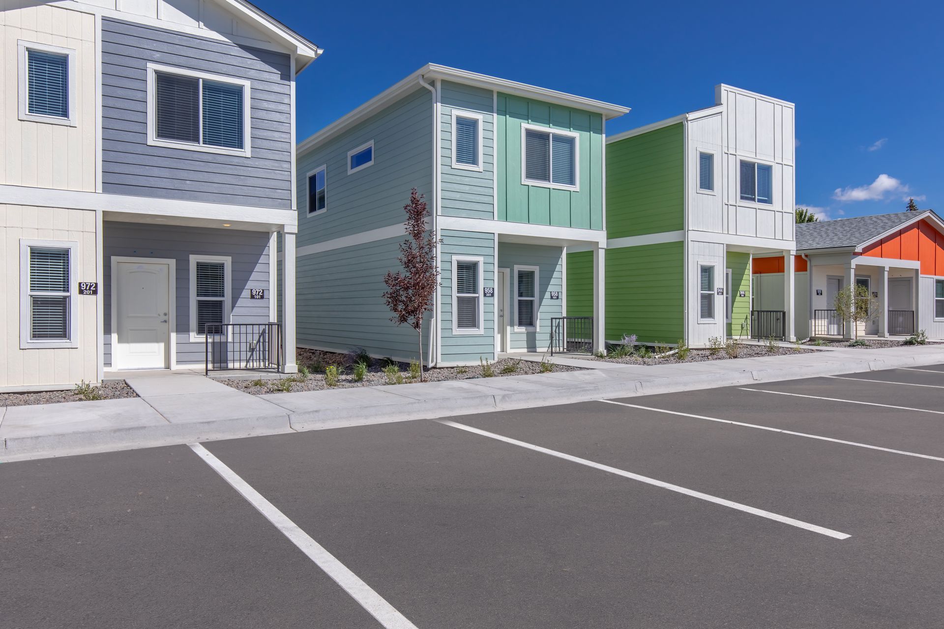 Colorful modern townhouses with white parking spaces in front under a clear blue sky