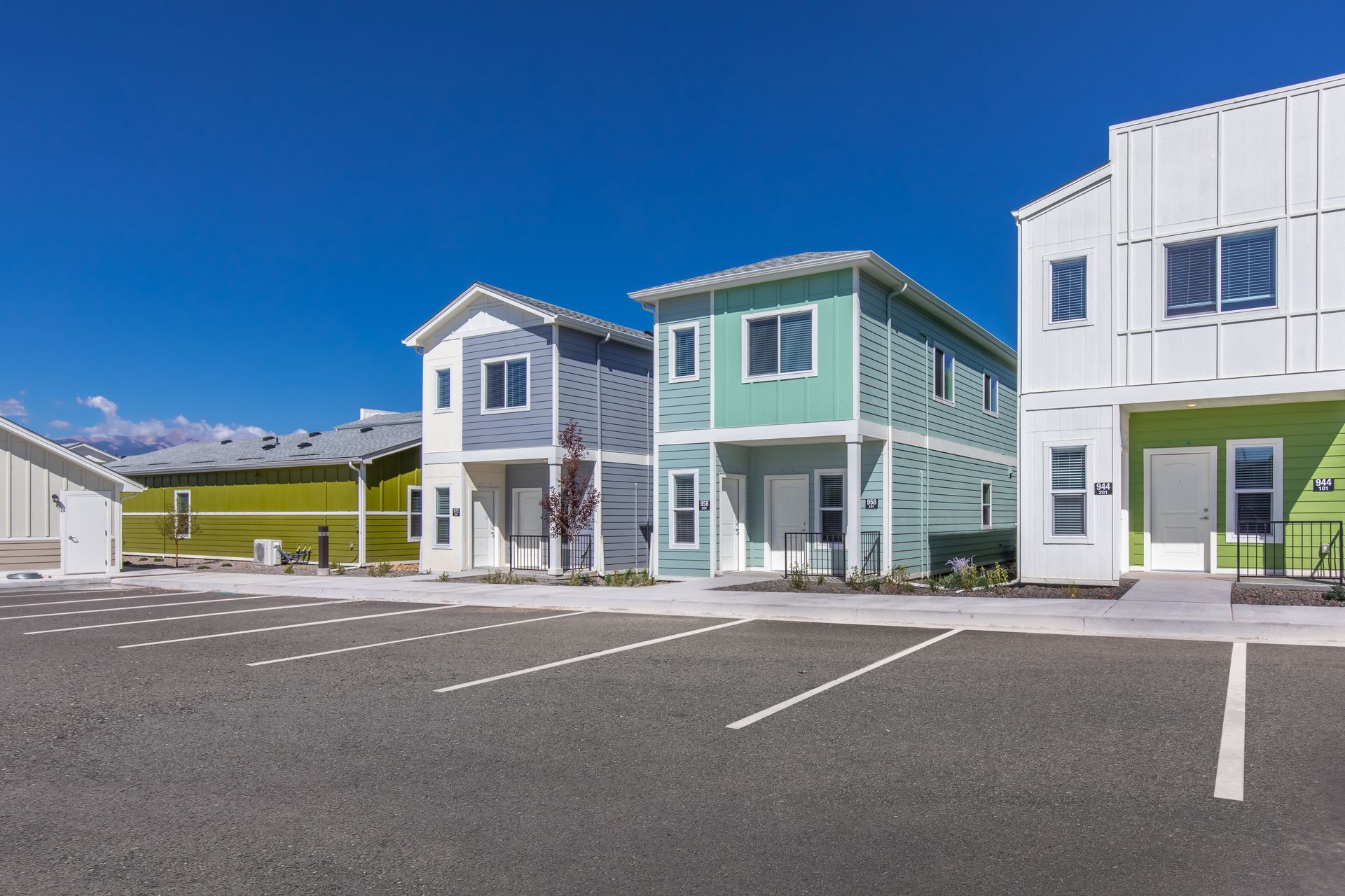 Colorful modern houses with empty parking spaces under a clear blue sky.