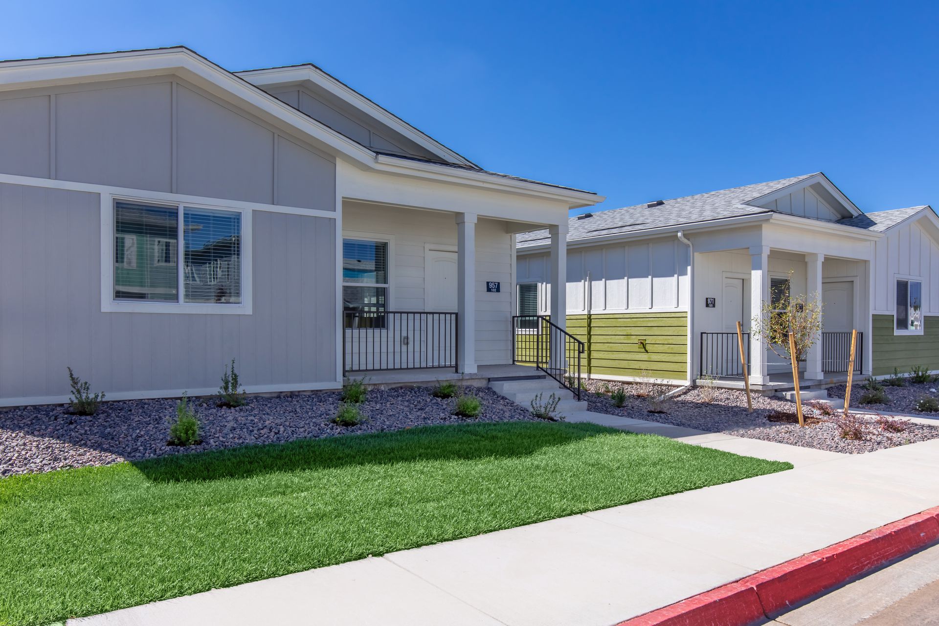 Single-story beige house with a small front lawn, walkway, and carport under a clear blue sky