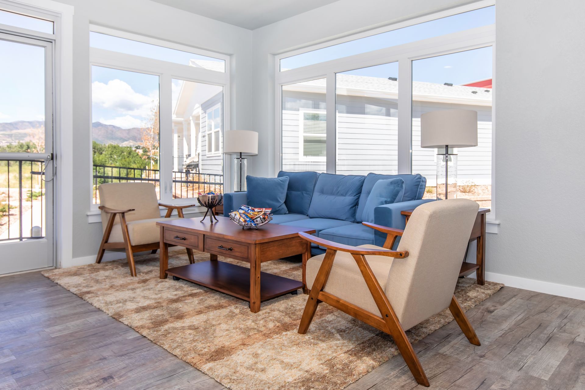 Bright living room with blue sofa, wooden coffee table, chairs, and large windows overlooking a balcony.