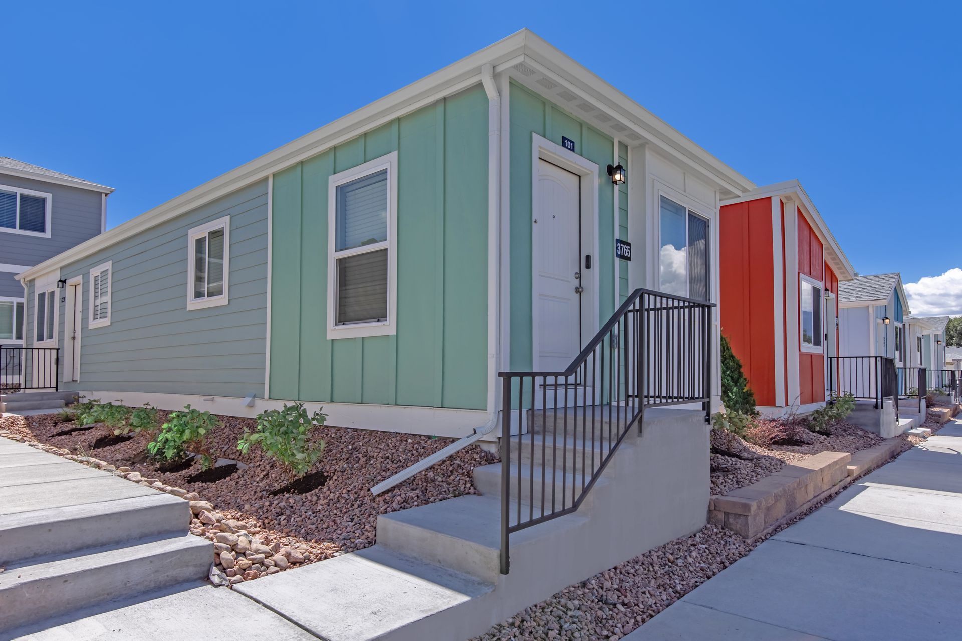 Modern modular home exterior with mint green siding, red accent panel, and front steps with black railing