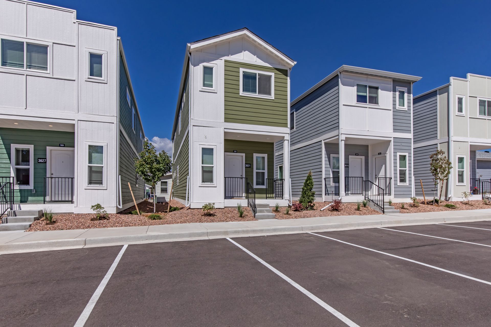 Row of modern townhouses with white and green exteriors beside an empty parking lot