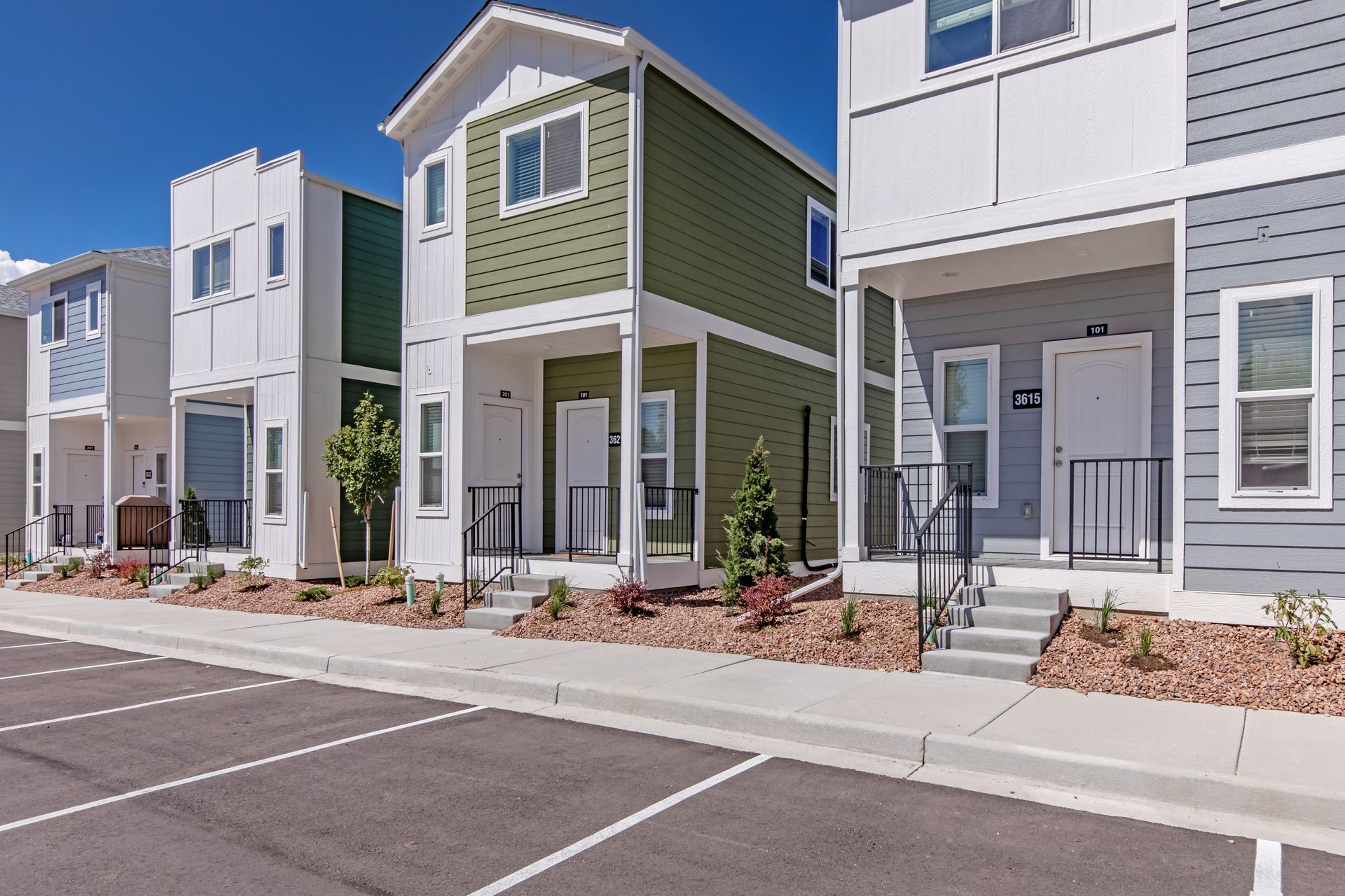 Row of modern townhomes with colorful facades along a parking lot and sidewalk