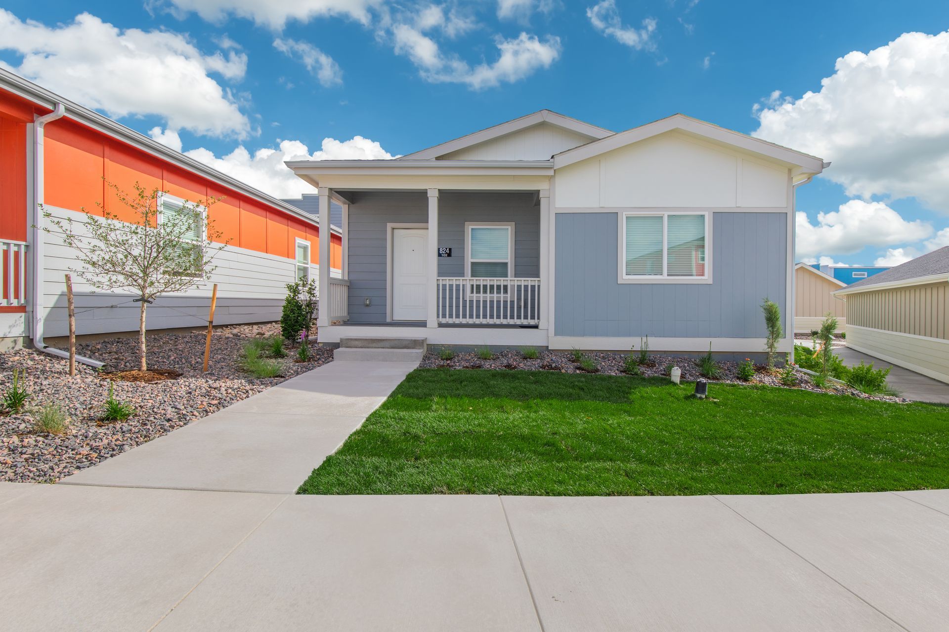 Modern single-story house with gray siding, white trim, a front porch, and a green lawn under a blue sky