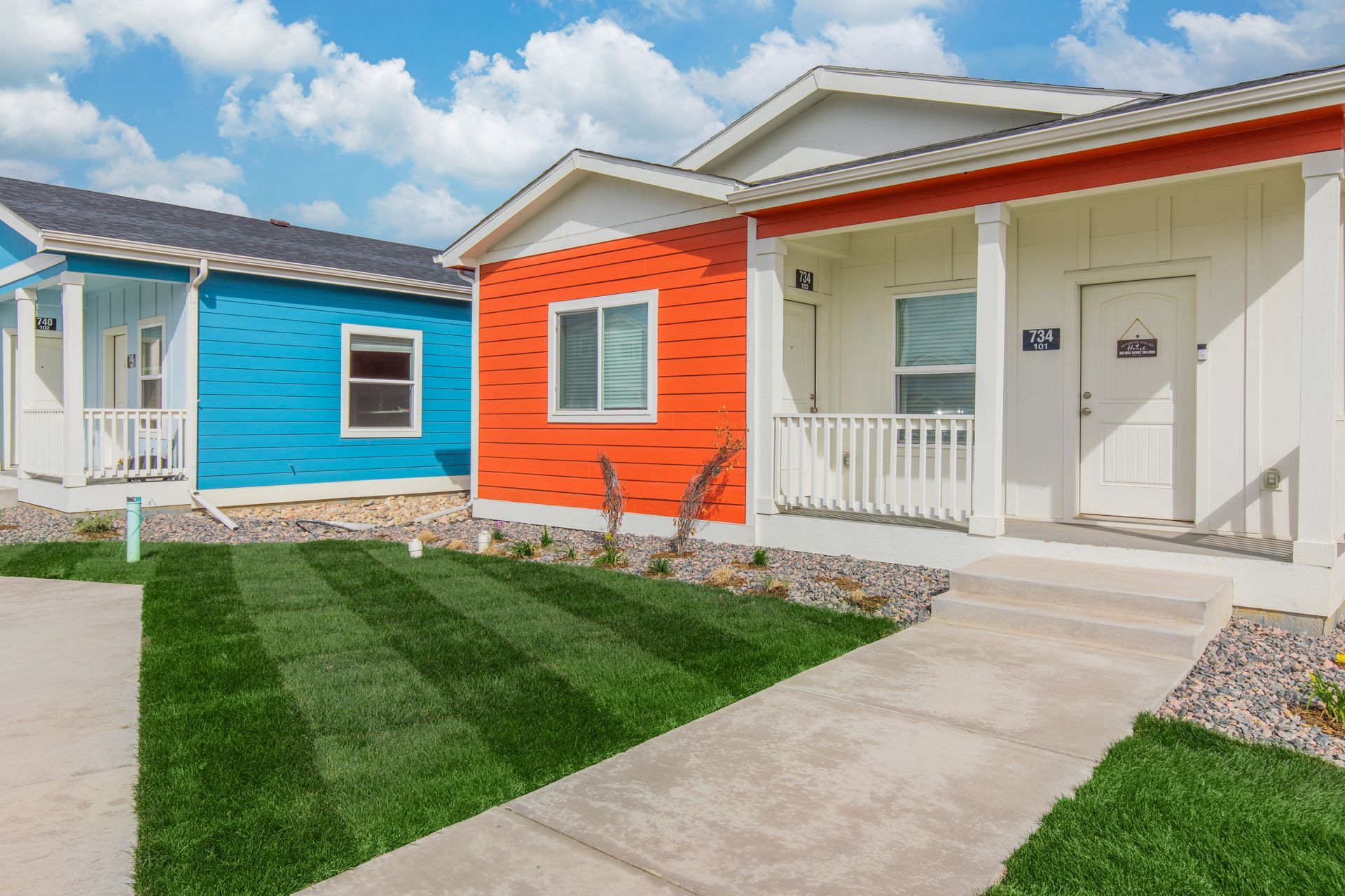 Colorful modern houses with white trim and small front lawns along a sidewalk