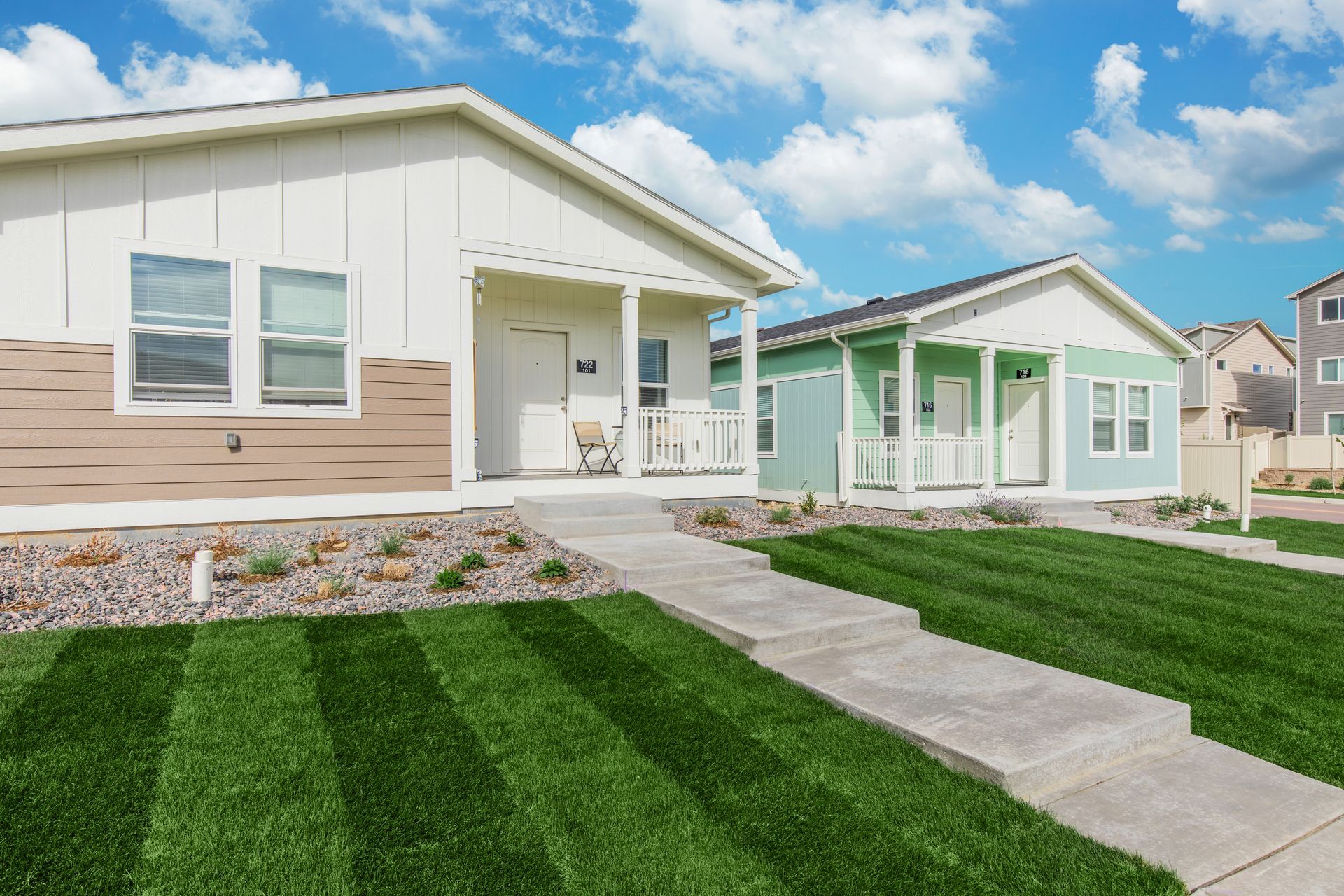 Modern single-family homes with manicured lawns and a concrete walkway under a blue sky