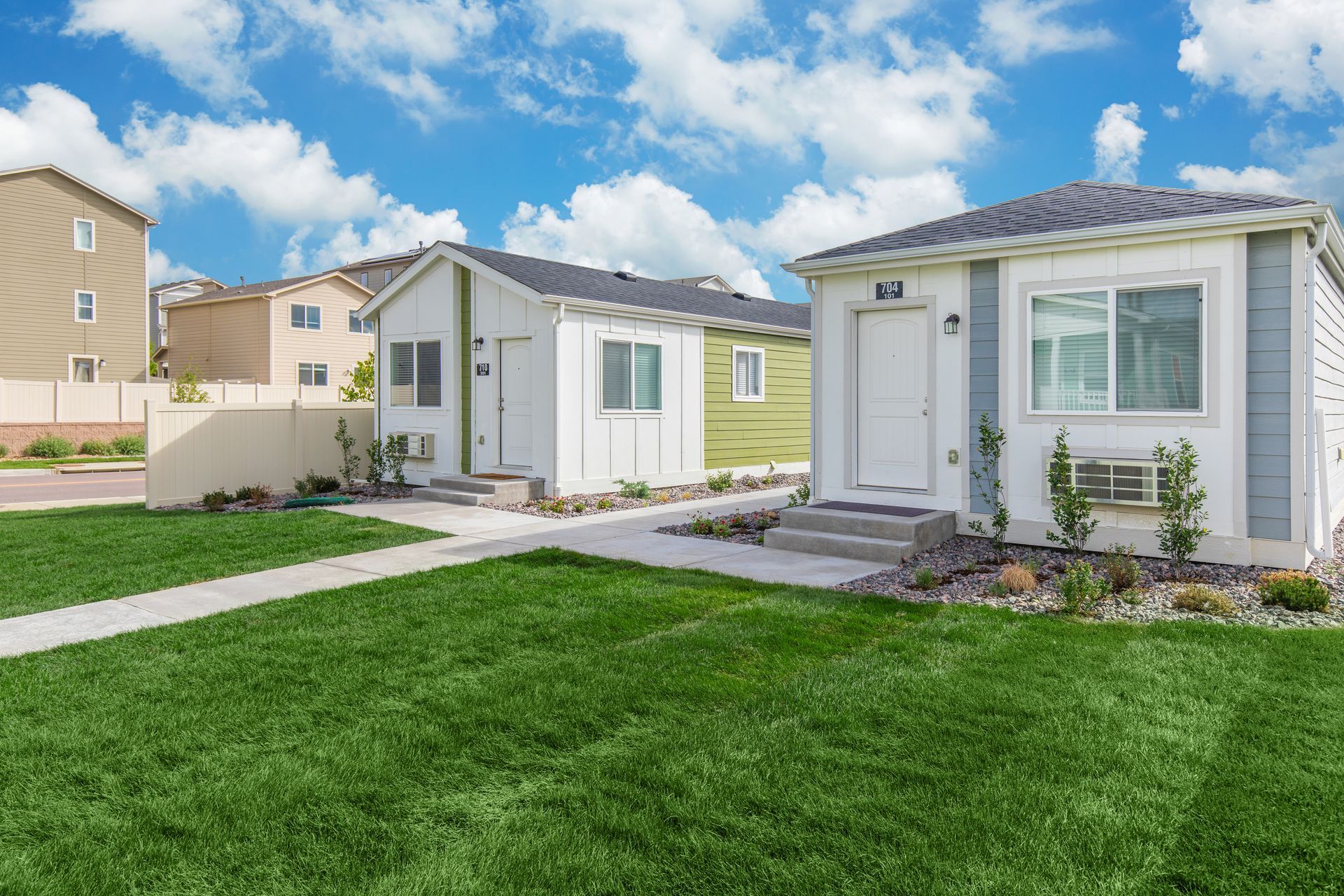 Two small white homes with front porches beside a green lawn under a blue sky