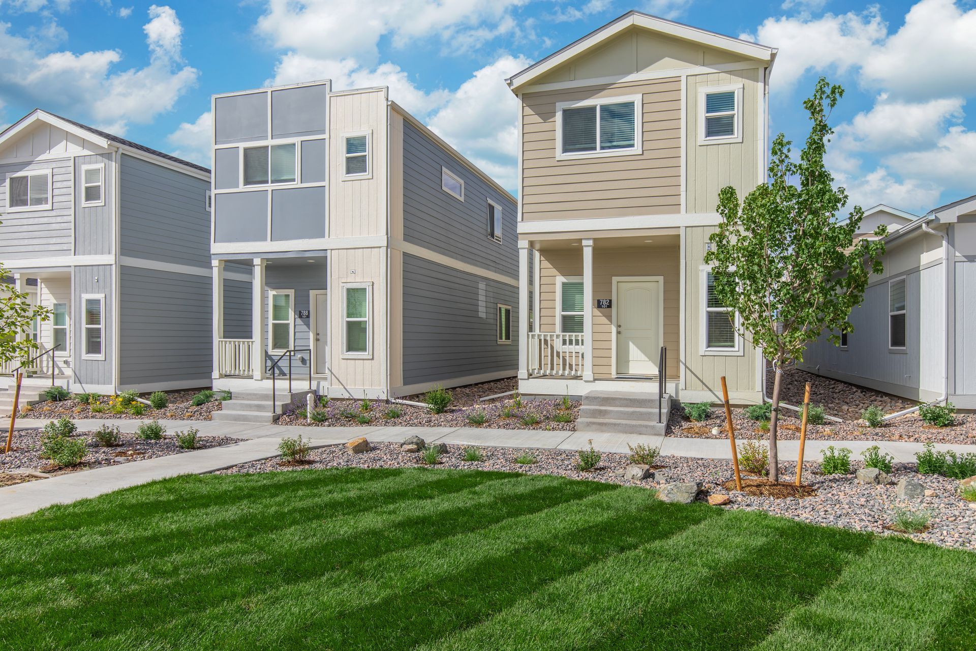 Row of modern townhouses with a manicured green lawn under a blue sky