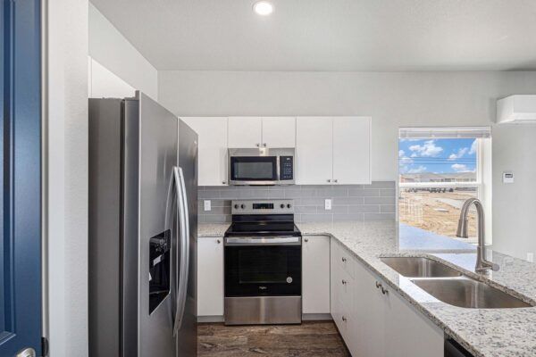 Modern kitchen with white cabinets, stainless appliances, and a large window over a double sink