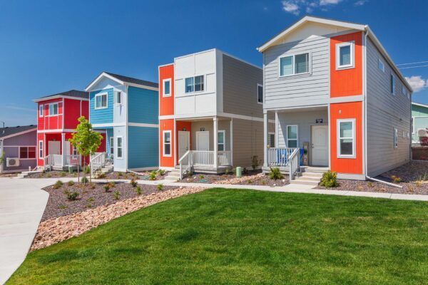 Row of colorful modern townhouses with green lawn and paved walkway under a bright sky