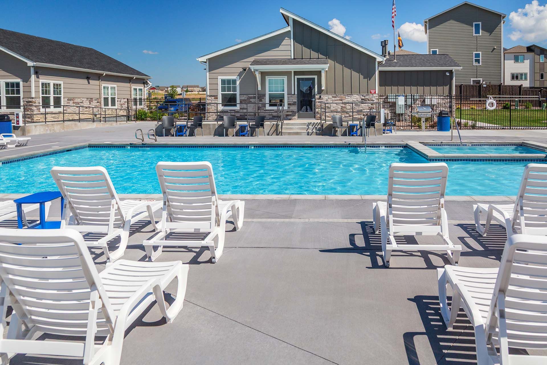 Outdoor swimming pool with white lounge chairs and a clubhouse in the background