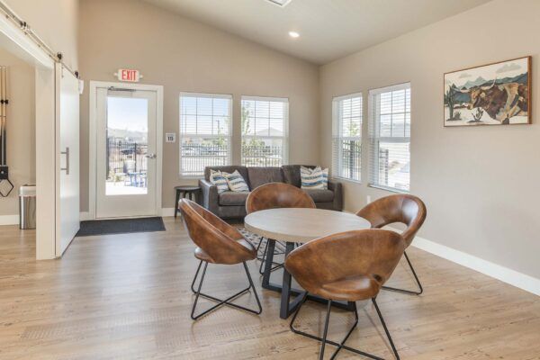 Modern lounge with round table, brown chairs, sofa, windows, and a glass door in a bright room