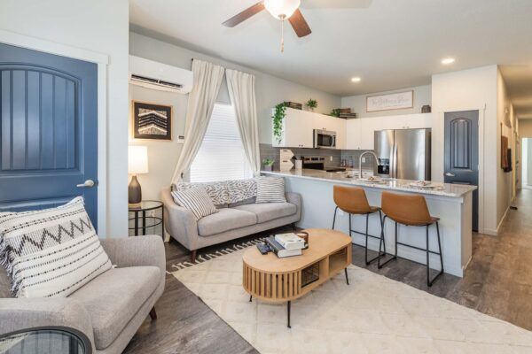 Bright modern living room with gray sofa, bar stools, coffee table, and open kitchen