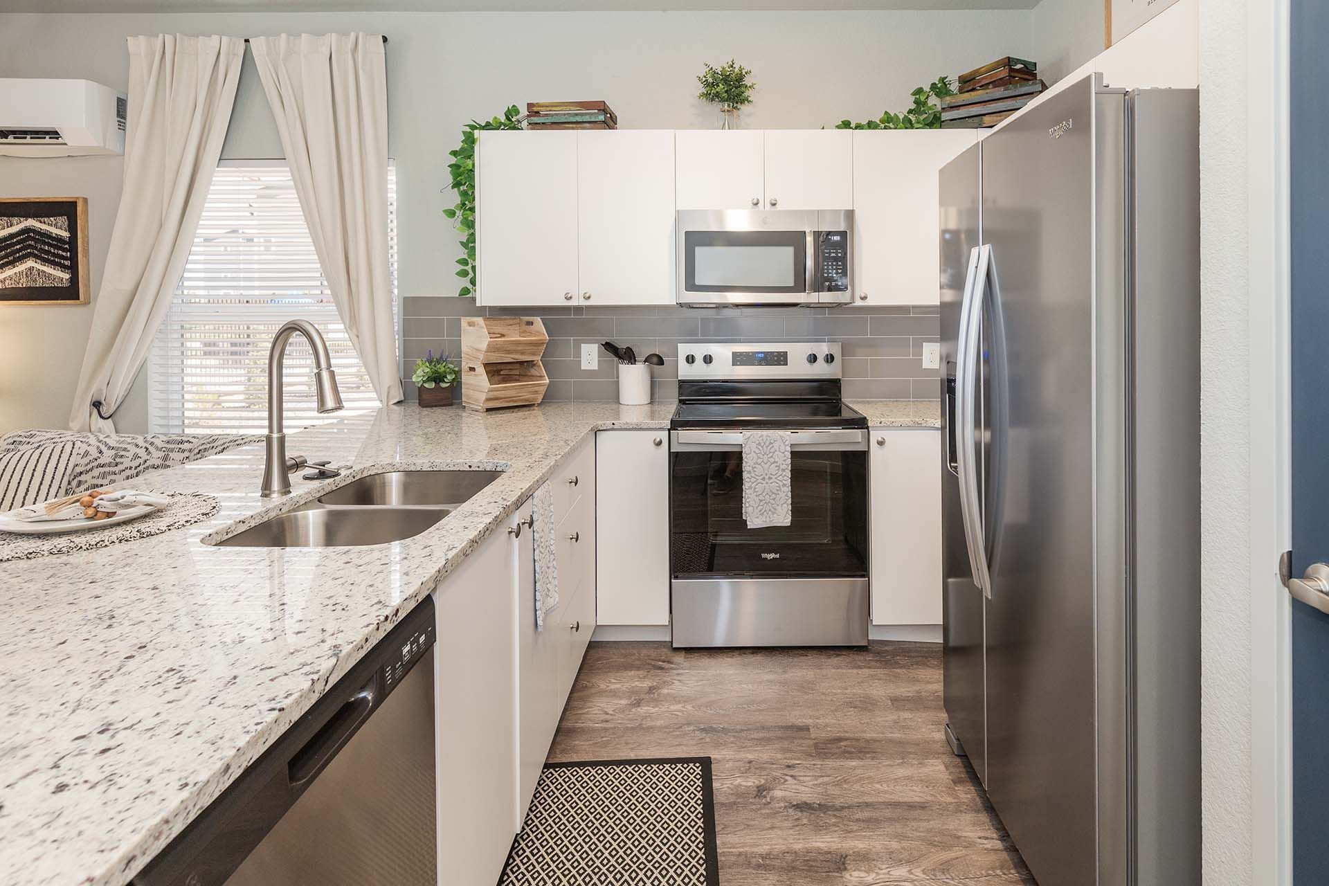 Bright modern kitchen with white cabinets, granite counters, stainless appliances, and a center aisle