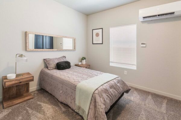 Small bedroom with a single bed, nightstand, wall mirror, window, and air conditioner.