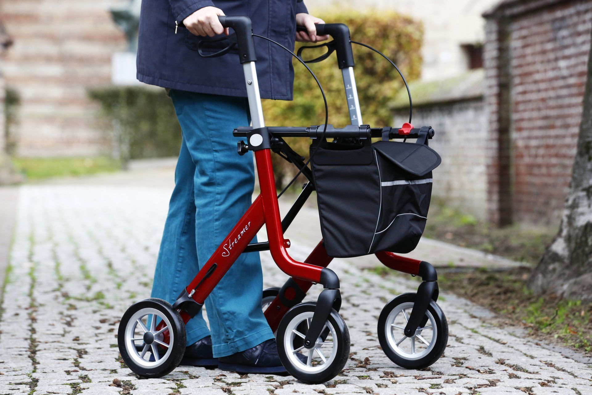 Iemand loopt met een rode rollator op de stoep.