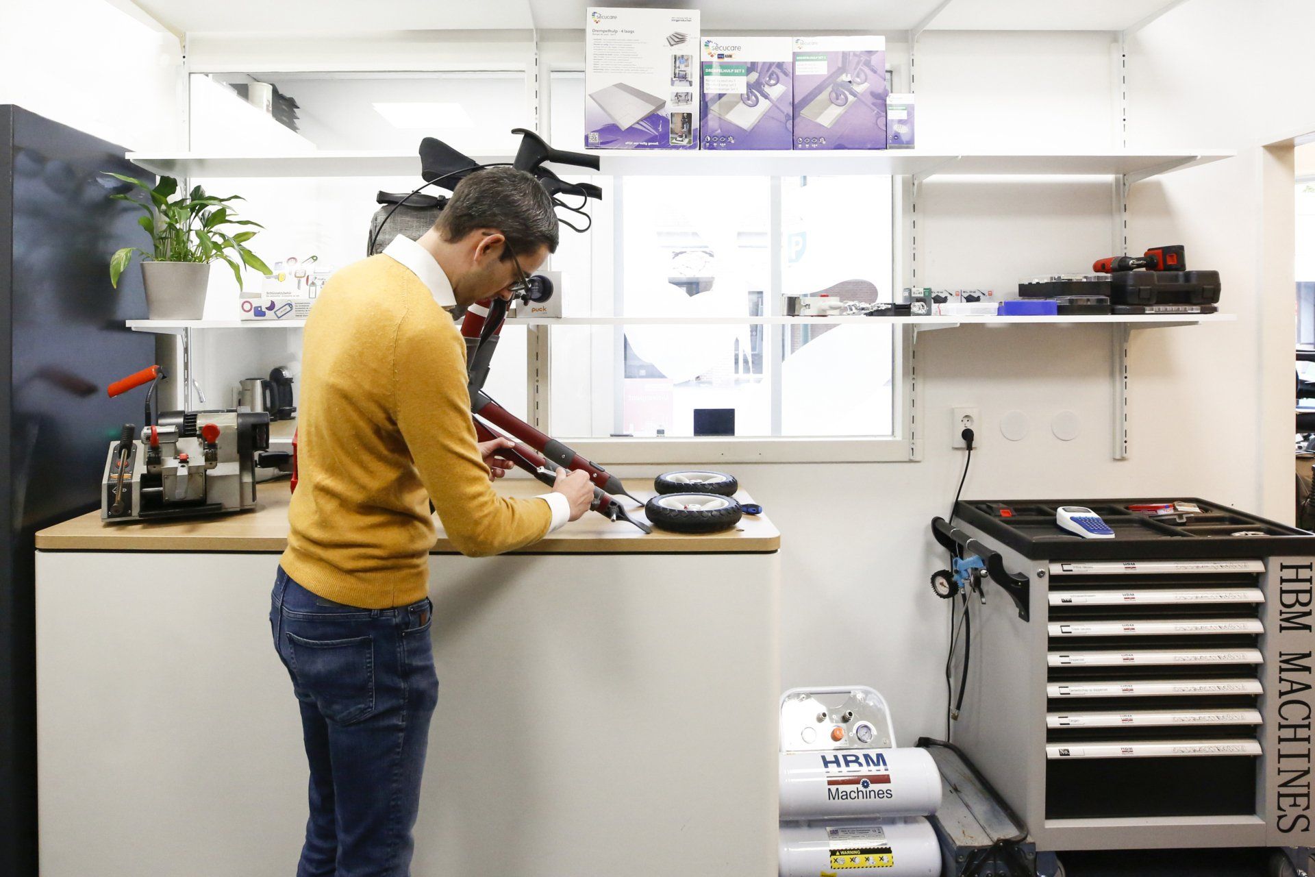 Een man in een gele trui werkt aan een machine in een werkplaats.