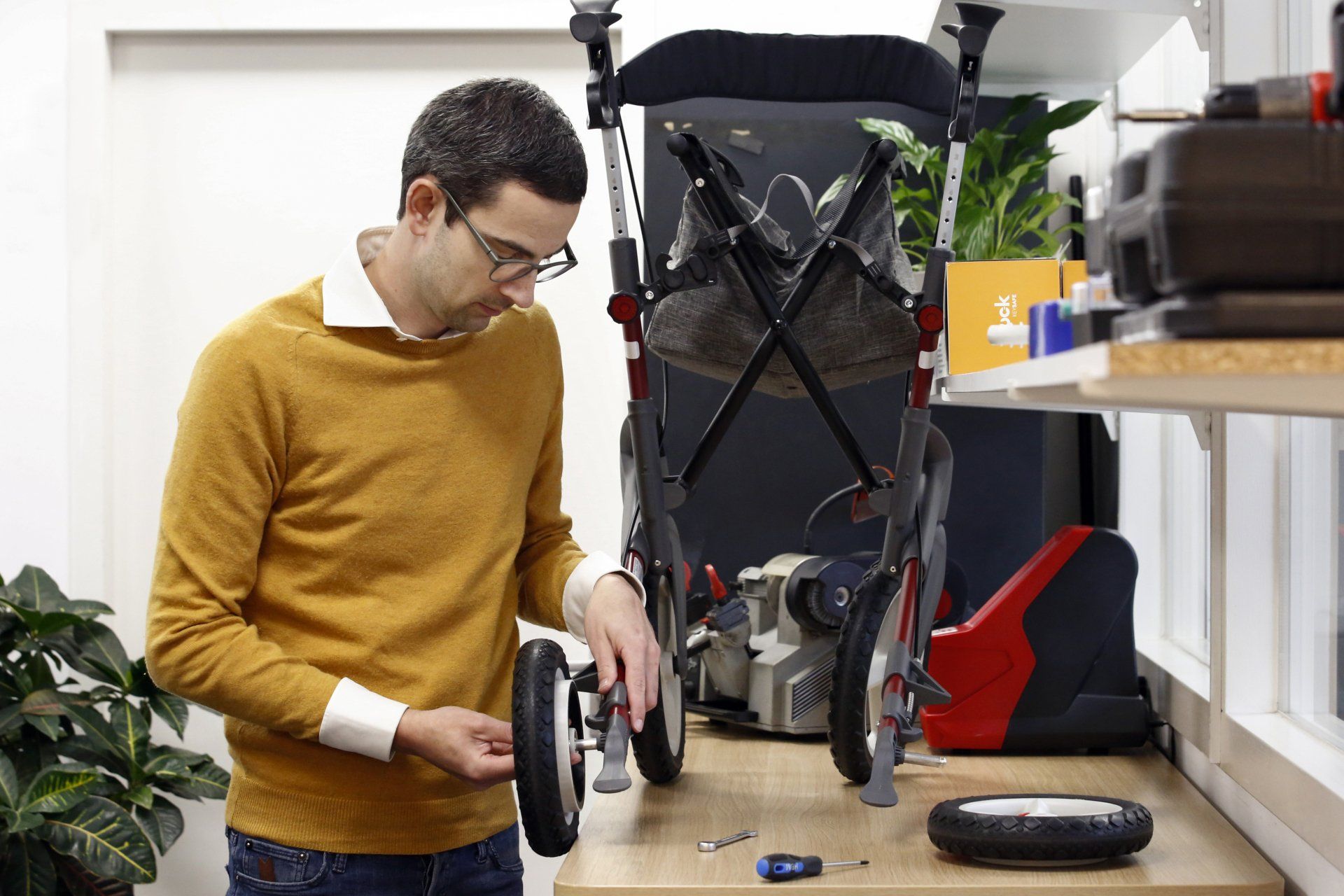 Een man in een gele trui werkt aan een kinderwagen.