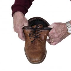 Een persoon strikt de veters van een paar bruine leren schoenen.
