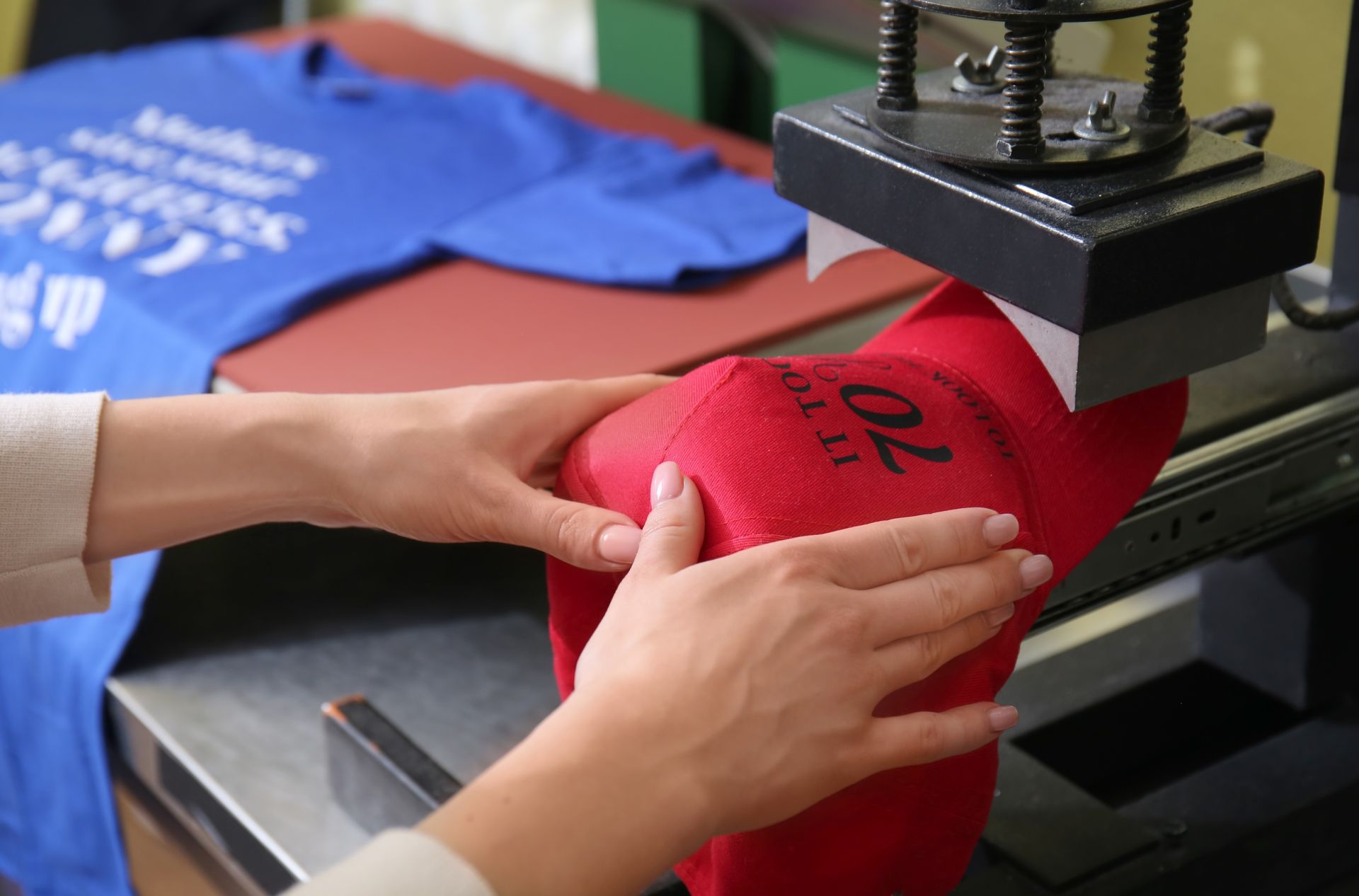 Hands positioning a red shirt under a heat press in a clothing print shop