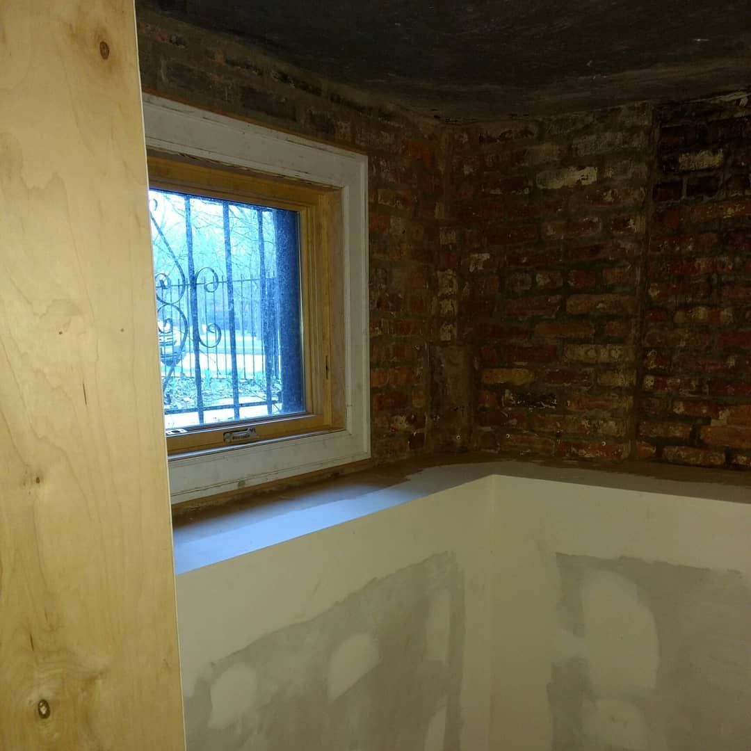 Window in a brick-walled basement with white trim, view through barred window.