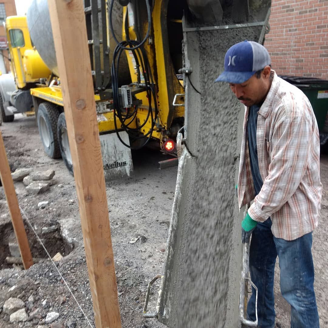 Man using a tool to smooth concrete pouring from a truck into a form. Construction site setting.