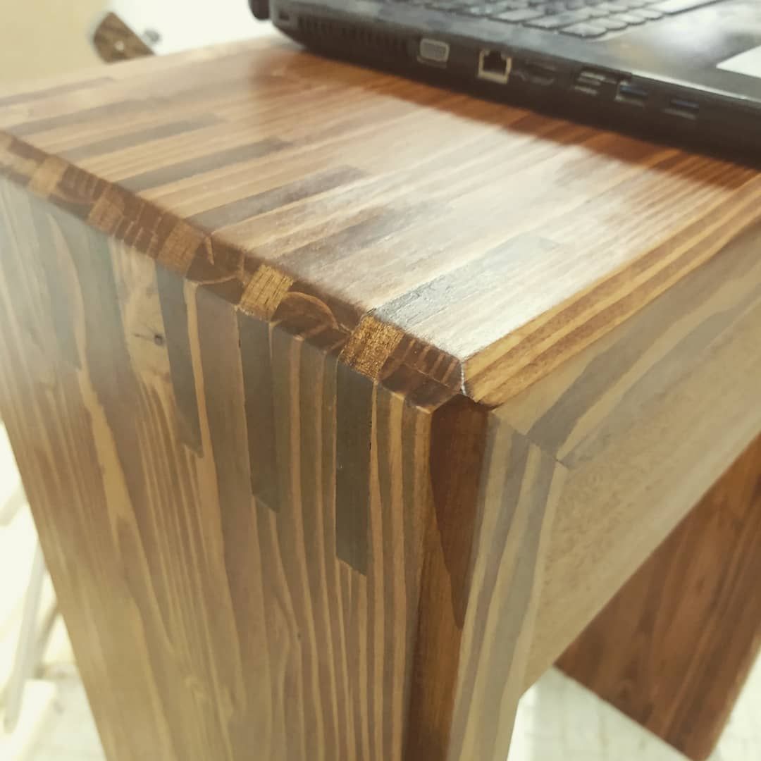 Close-up of a wooden table corner with a laptop. Brown wood grain, glossy finish.