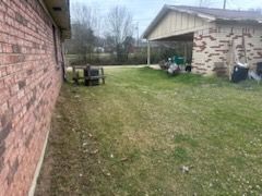 Backyard lawn between brick house walls, with a covered patio and picnic table in the background