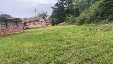 Grassy yard beside a brick house and small outbuilding under overcast sky