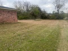Grassy backyard beside a brick house with trees and cloudy sky