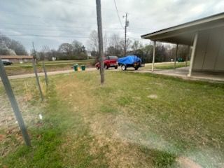Rural yard with a red car and blue tarp-covered vehicle near a carport, under overcast skies