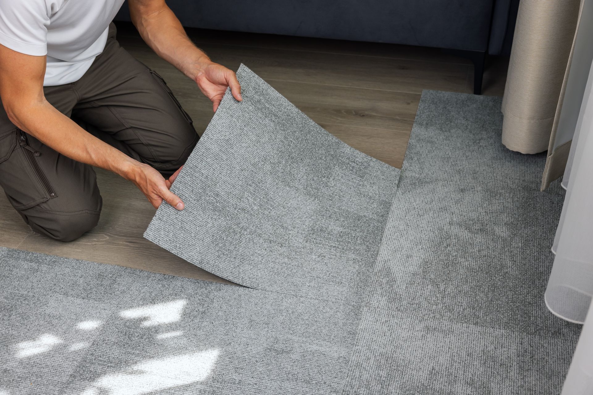 A man is kneeling on the floor holding a piece of carpet.