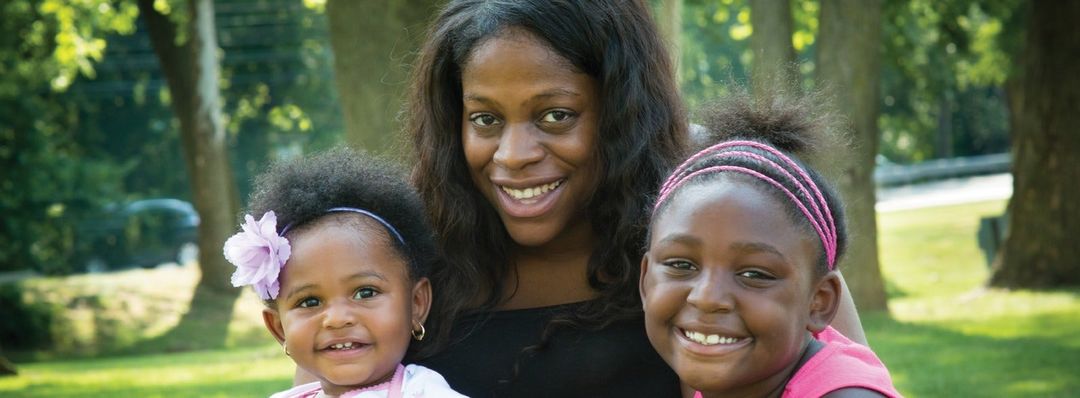 A woman is holding two little girls in her arms in a park.