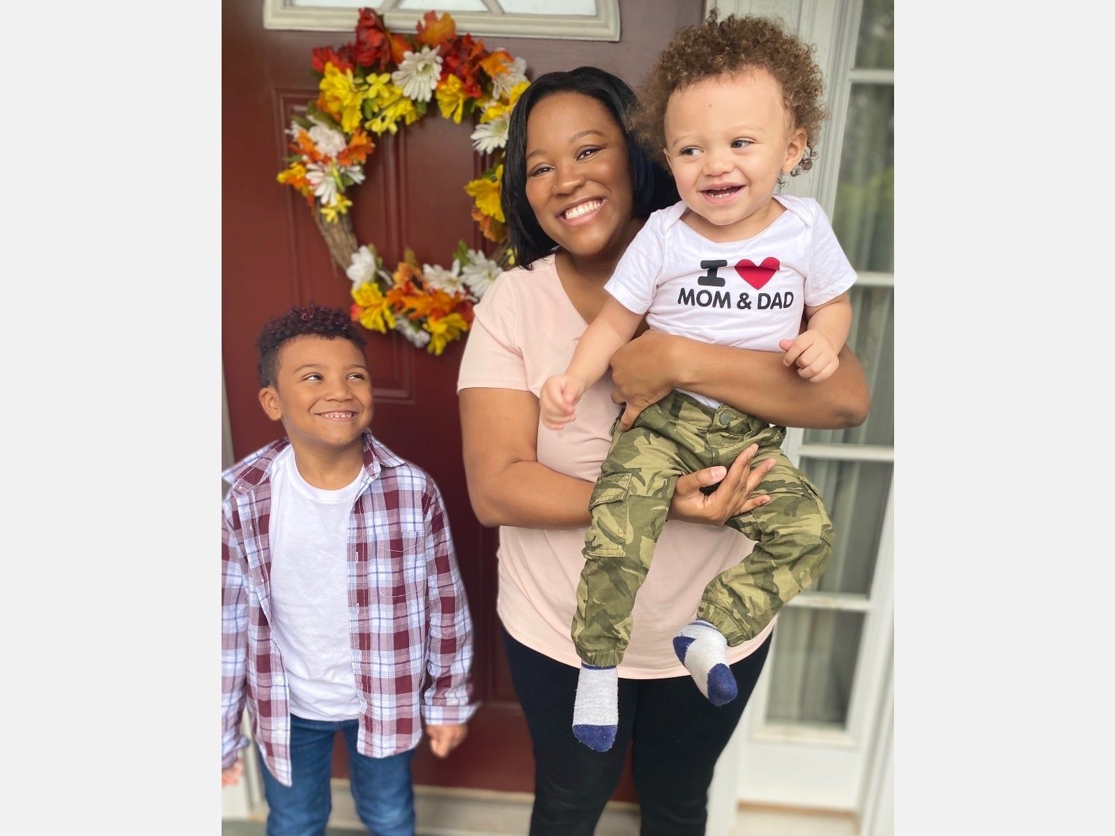 A woman is holding a baby and two boys are standing in front of a door.
