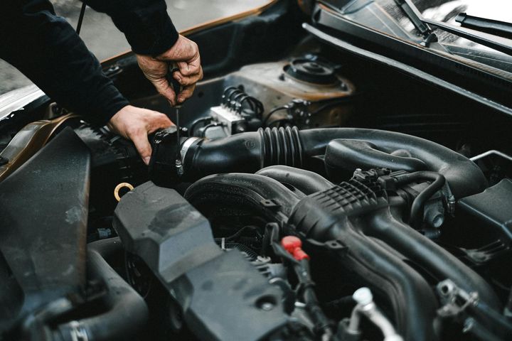 Mechanic working on a car engine with hands and tools.