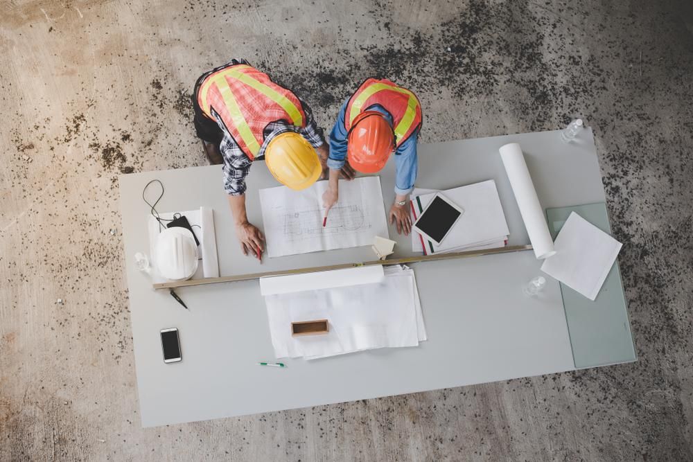 Two Construction Workers Are Looking at A Blueprint on A Table — Duggan Mather Surveyors in Taylors Beach, NSW