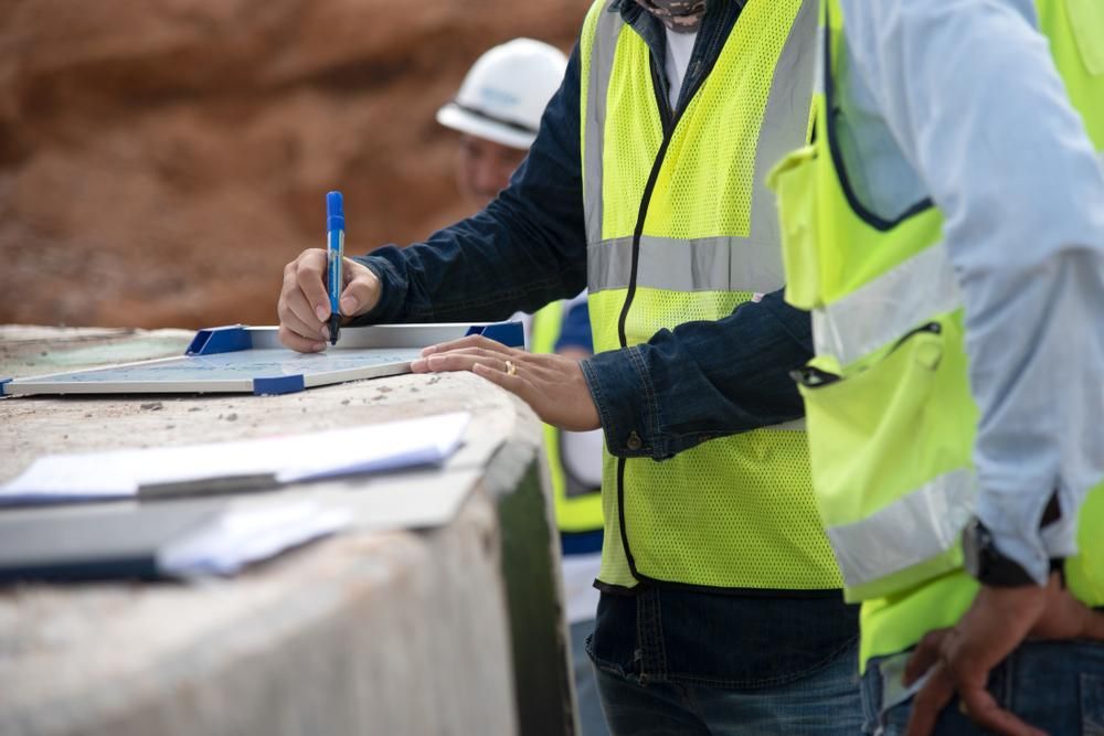 A Man in A Yellow Vest Is Writing on A Piece of Paper — Duggan Mather Surveyors in Taylors Beach, NSW
