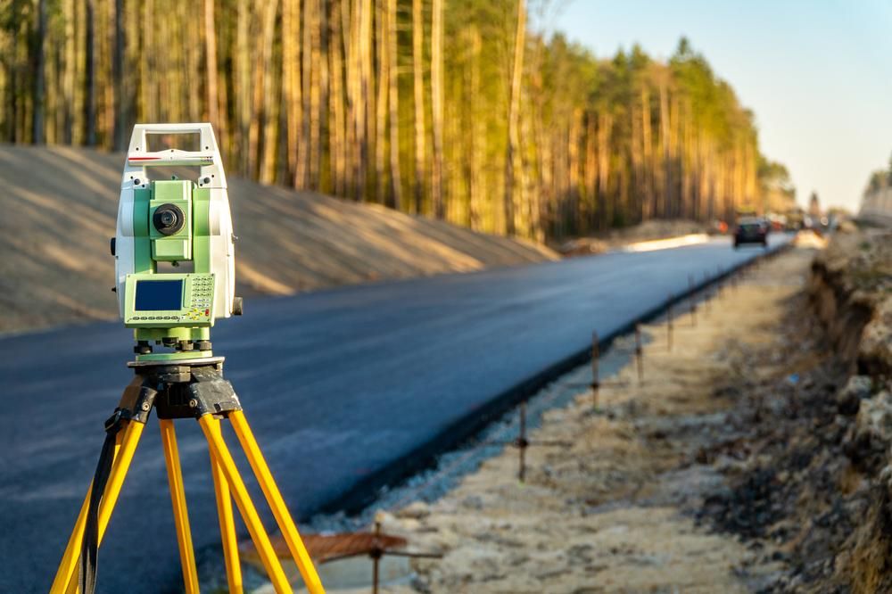 A Total Station Is Sitting on A Tripod on The Side of A Road — Duggan Mather Surveyors in Taylors Beach, NSW