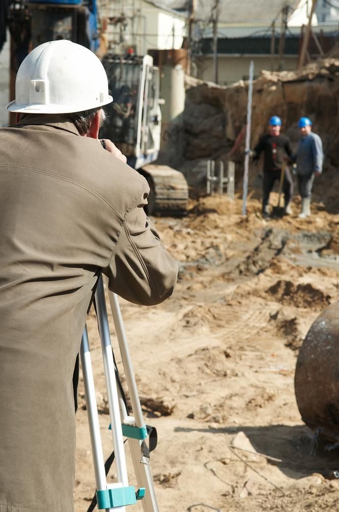 A Man Wearing a Hard Hat Is Taking a Picture of A Construction Site — Duggan Mather Surveyors in Taree, NSW