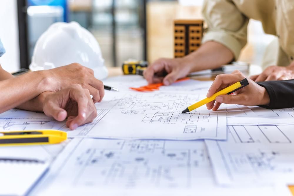 A Group of People Are Sitting at A Table Looking at A Blueprint — Duggan Mather Surveyors in Taylors Beach, NSW