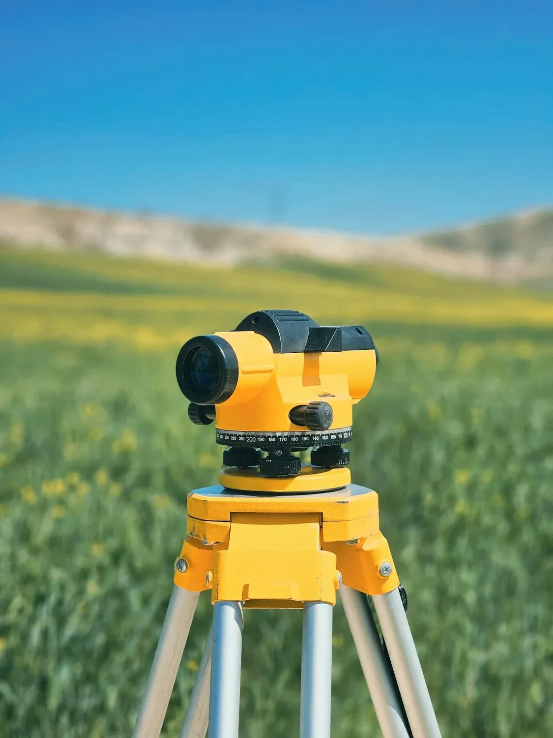 A Yellow Level Is Sitting on Top of A Tripod in A Field — Duggan Mather Surveyors in Taylors Beach, NSW