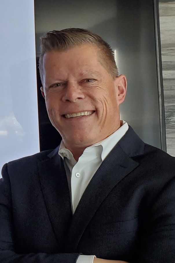A man in a suit and white shirt is smiling for the camera.