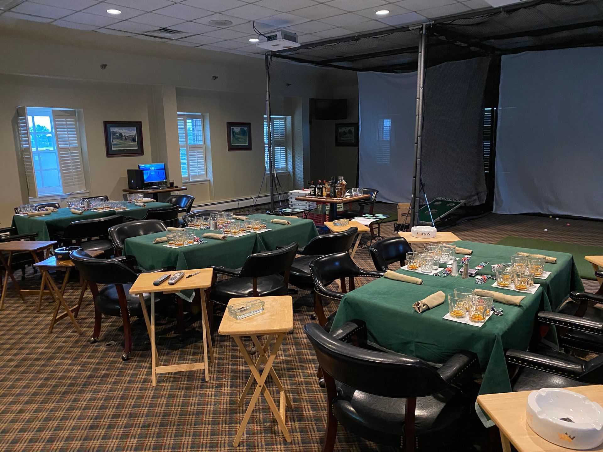Tables set for a gathering in a room with a golf simulator net in the corner.