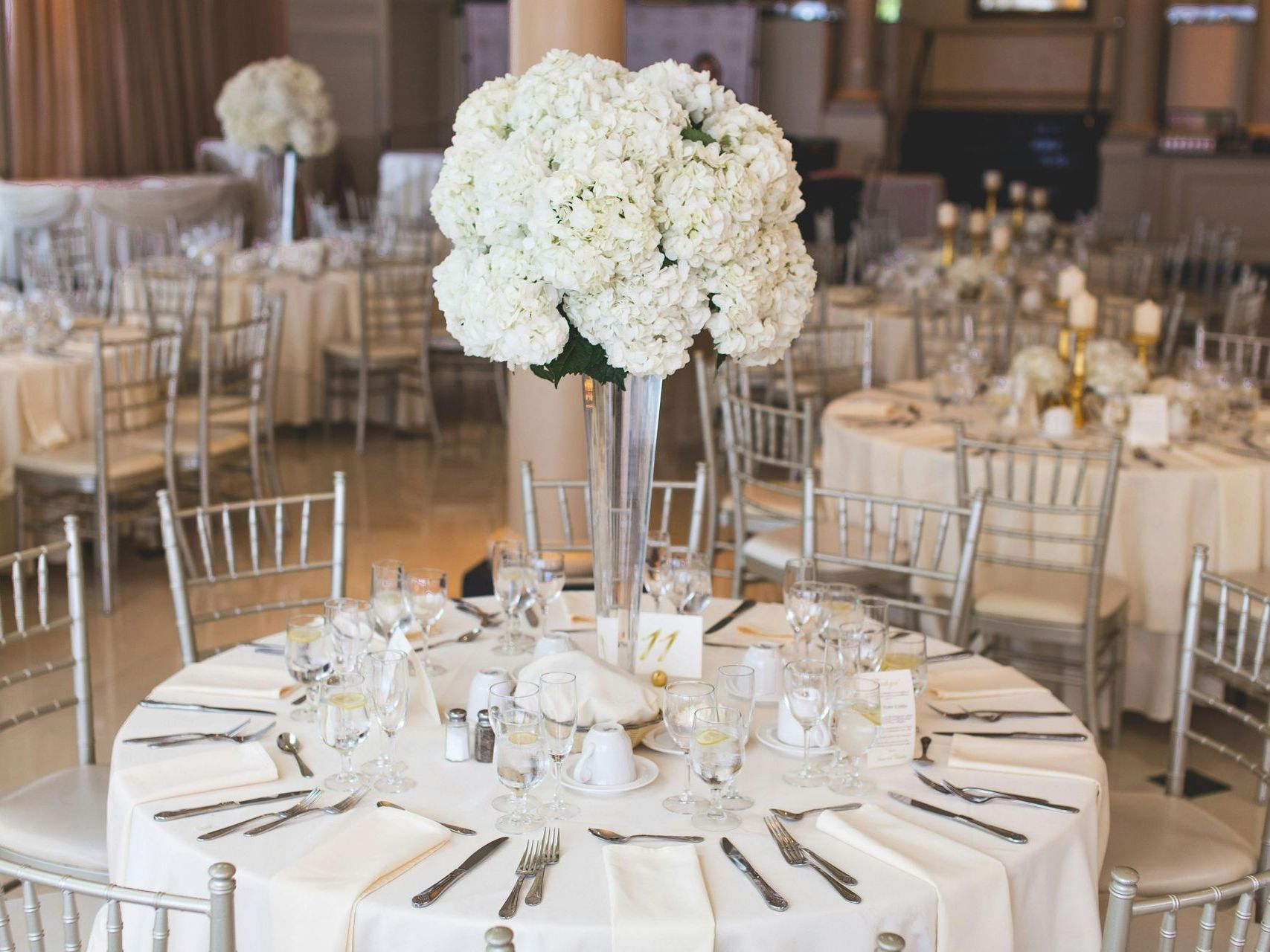 A large vase filled with white flowers is on a table at a wedding reception.