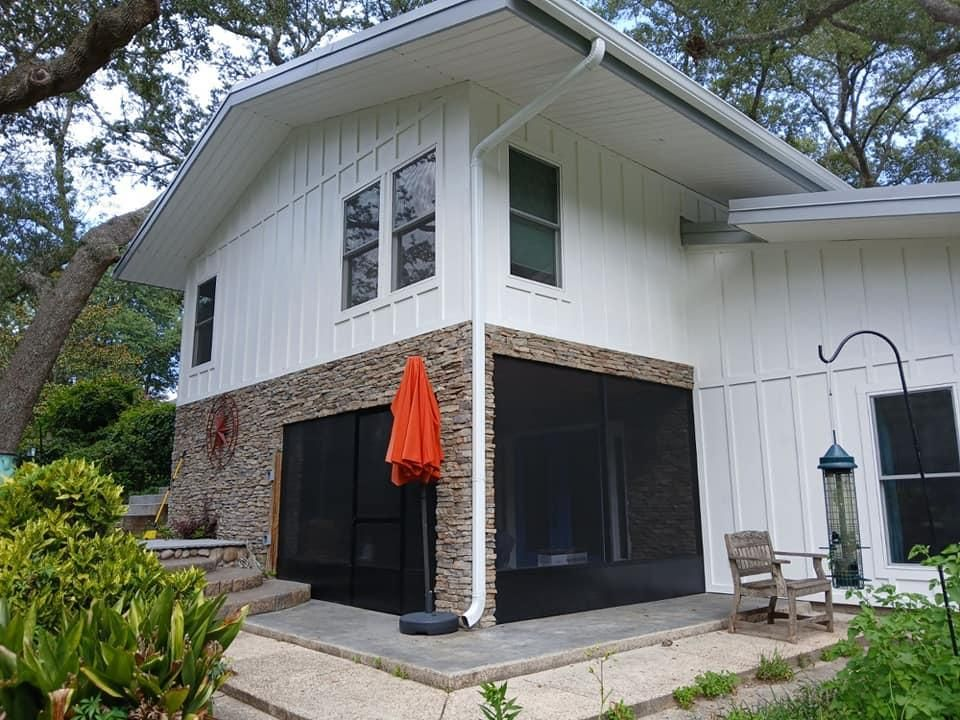 Two-story white house with stone base, screened porch, orange umbrella, and green plants.