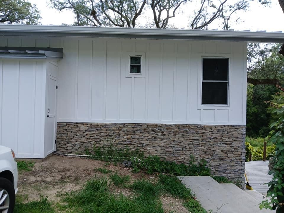 White building with stone base, small window, and driveway.
