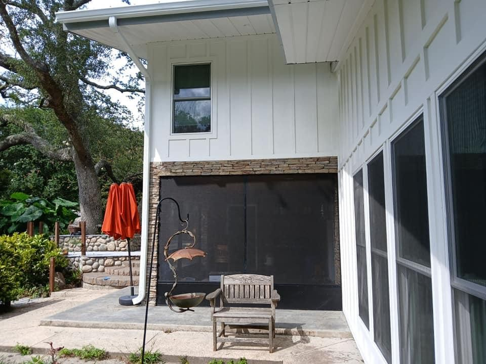 White house exterior with screen porch, chair, and orange umbrella.
