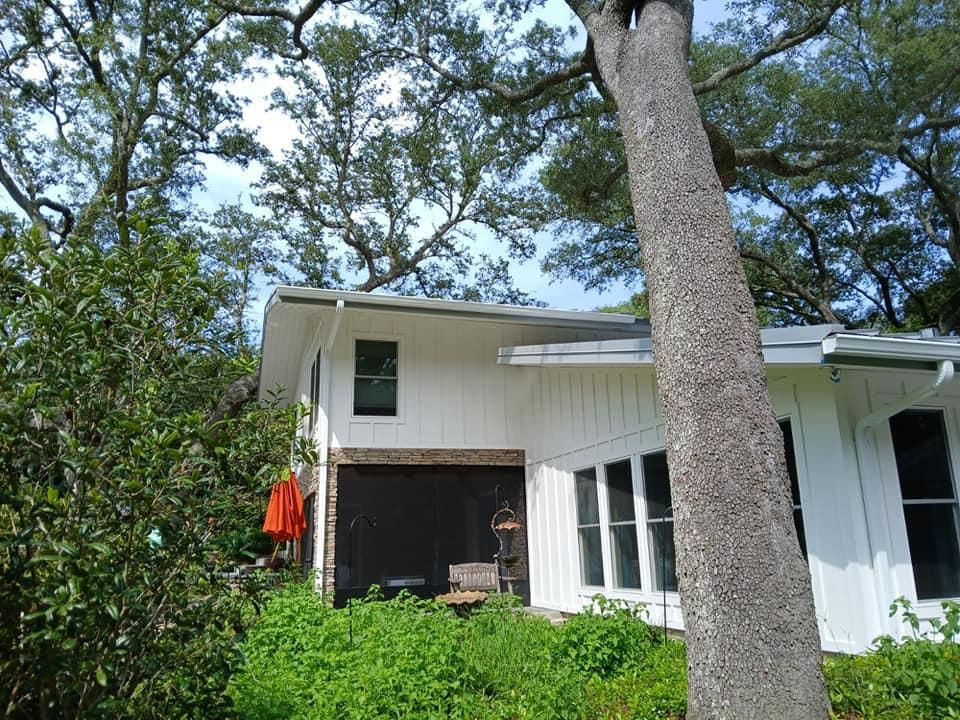 White house with dark garage, windows, and surrounded by trees and green bushes.