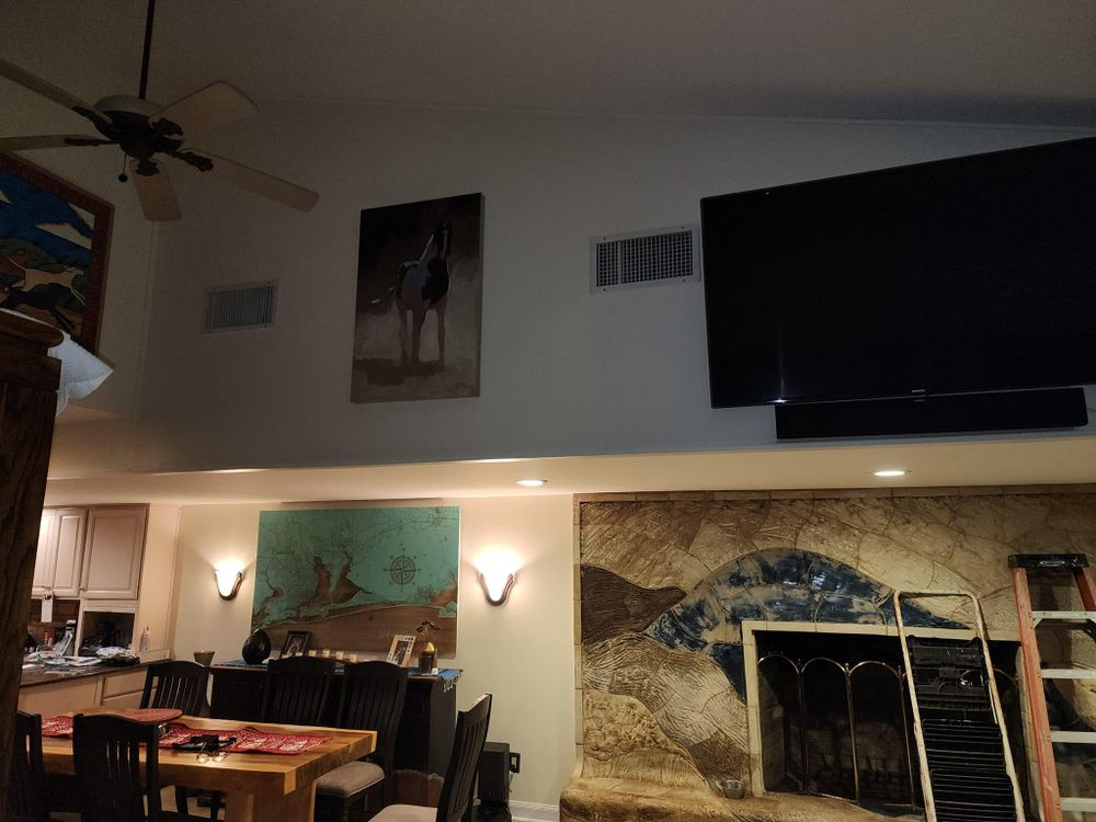 Living room with high ceiling, art, fireplace, and large TV mounted above a soundbar.